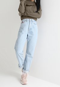 Light blue high-waisted jeans, fitted at the waist, relaxed through the legs. Paired with a dark olive green zip-up hoodie and pink sneakers.