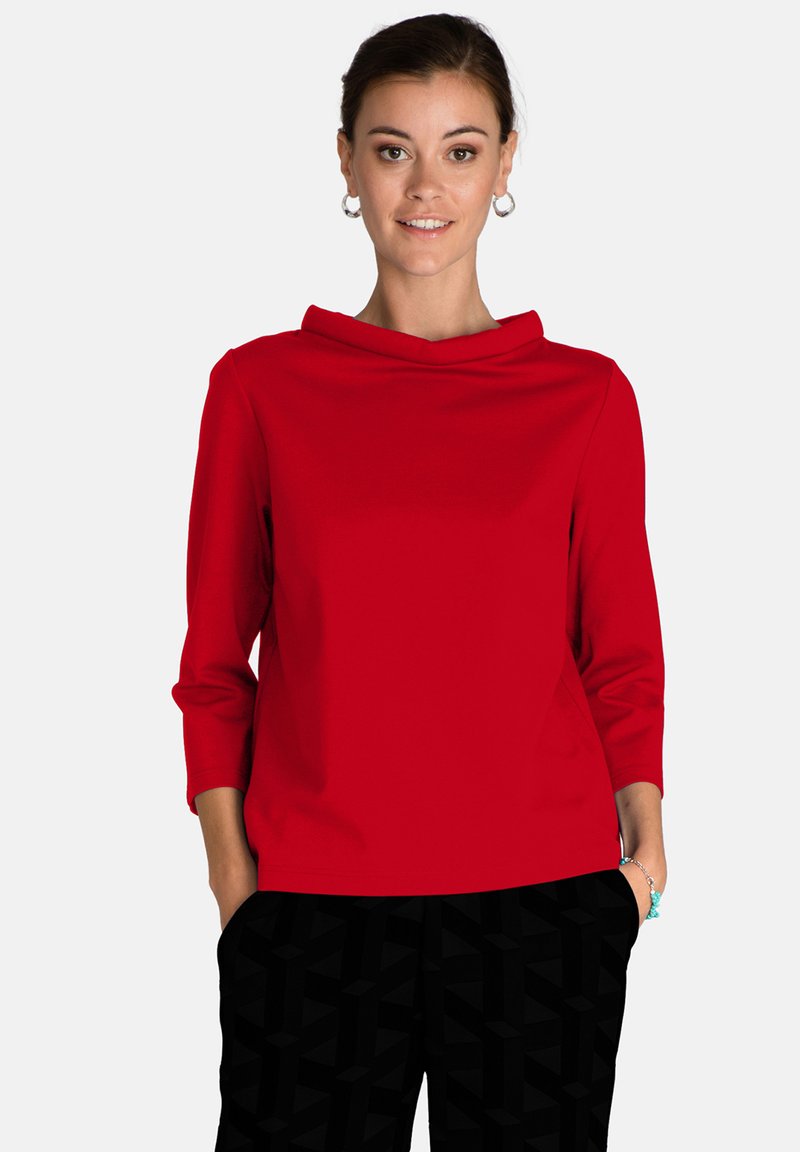 Top rosso aderente con collo a cappuccio e maniche tre quarti, realizzato in un tessuto liscio e elastico. Abbinato a pantaloni neri con motivo.