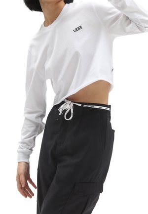 Person wearing a white long-sleeve Vans crop top and black pants with a Vans-branded waistband and drawstring, posing with one arm raised.