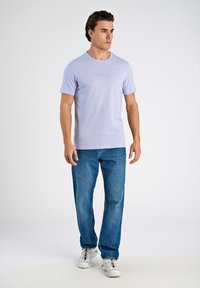 Ljuslila kortärmad t-shirt med rund hals och diskret varumärkeslogga, matchad med blå raka jeans och vita sneakers.