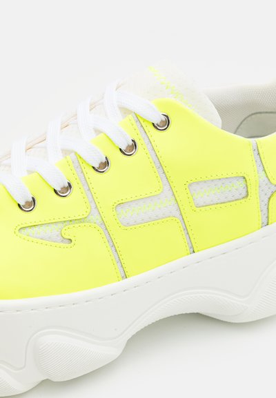 Νεον κίτρινα αθλητικά παπούτσια με λευκές σόλες, κατασκευασμένα από απαλό συνθετικό υλικό, με κεντημένα διακοσμητικά στοιχεία και μεταλλικές οπές για τα κορδόνια.