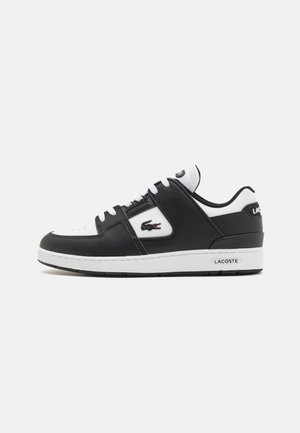 Black leather sneaker with white accents, round toe, lace-up closure, textured body, and Lacoste logo on the side. Rubber sole.