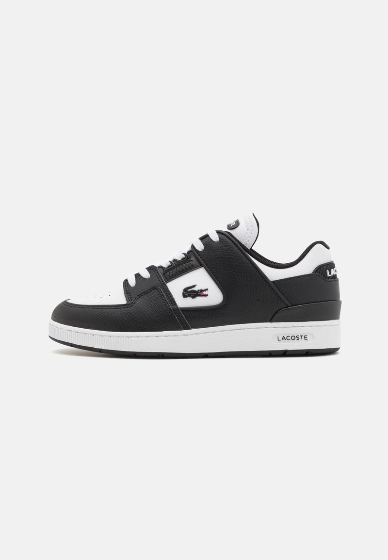 Zapatilla negra de cuero con acentos blancos, puntera redonda, cierre con cordones, cuerpo texturizado y logo de Lacoste en el lateral. Suela de goma.