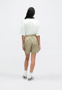 Rövid ujjú fehér galléros póló fekete gallérral, bézs rövidnadrággal párosítva. A ruhát szürke tornacipő és fehér zokni teszi teljessé.