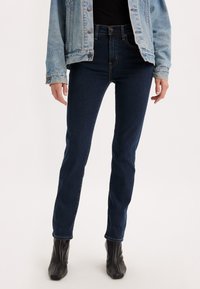 Jeans a vita alta blu scuro in un taglio slim, realizzati in denim con una texture liscia. Presentano tasche standard e dettagli di cucitura sottili.