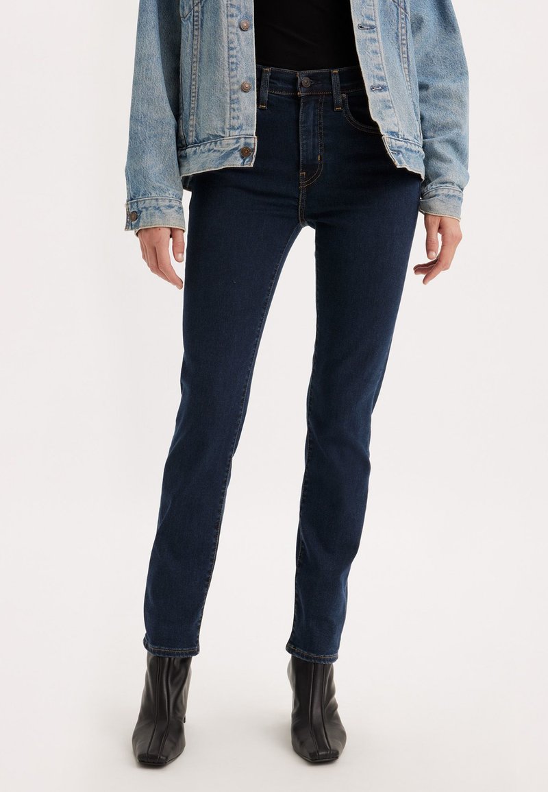 Jeans a vita alta blu scuro in un taglio slim, realizzati in denim con una texture liscia. Presentano tasche standard e dettagli di cucitura sottili.