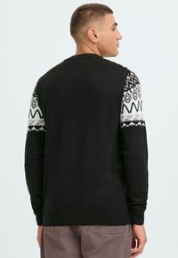 Schwarzer Strickpullover mit gemusterten weißen und grauen Akzenten an den Schultern. Gerippte Bündchen und Saum. Einfarbige Rückansicht mit einem runden Ausschnitt.