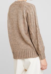 Ylimittainen ruskea neulepaita, jossa resorireuna ja teksturoidut palmikkokuvioidut hihat. Mukava ja lämmin villasekoitemateriaali.