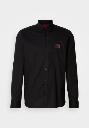 Camicia nera a maniche lunghe in tessuto liscio, con chiusura a bottoni, collo classico e una piccola patch con marchio rosso sul petto.