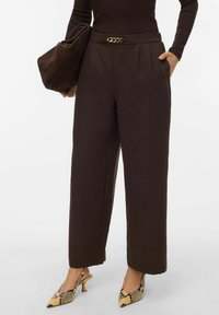 Pantalon ample marron avec ceinture à cha�îne dorée, associé à un sac marron et des chaussures à talons hauts à motif imprimé serpent.