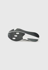 Semelle de chaussure de sport noir et blanc avec une texture antidérapante, dotée d'une semelle intermédiaire blanche lisse et de multiples découpes pour plus de flexibilité.