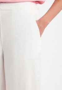 Weiße weit geschnittene Hose mit glatter Textur und einer Seitentasche, ausgestattet mit einem schlichten Bund. Einfaches und modernes Design.