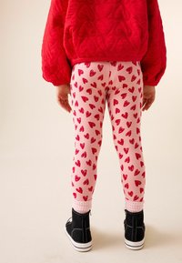 Suéter acolchado rojo con patrones de corazones; leggings rosas con pequeños corazones rojos; zapatos negros con suelas blancas; detalle de tela suave.