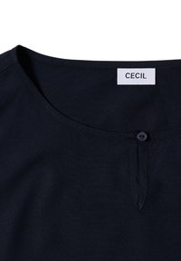 Blusa azul marino con cuello redondo, que presenta un cierre de botón y una textura de tela suave. La etiqueta dice "CECI".