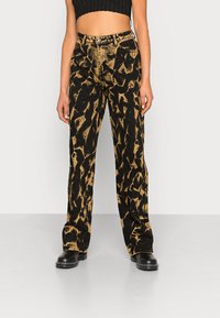 Schwarz-beige gemusterte Schlagjeans mit hoher Taille, die eine stark abgenutzte Textur und ein klassisches Fünf-Taschen-Design aufweisen.