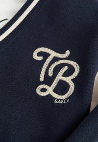 Navy brei trui met een crème geborduurd "TB" logo en de tekst "BAKER", met contrasterende crème strepen langs de halslijn.