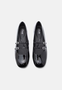 Par de sapatos Mary Jane de couro envernizado preto com fechos duplos e palmilhas almofadadas, fotografados de cima sobre um fundo branco.