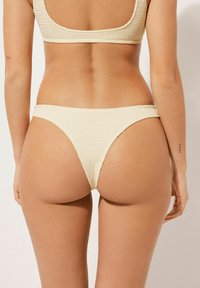 Krämfärgad bikini-set med texturerad tyg, top med rundad rygg och låg midja med minimal täckning och sömlösa kanter.
