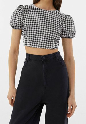 Femme portant un crop top à manches bouffantes à carreaux noirs et blancs, associé à un pantalon large noir taille haute.
