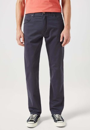 Pantaloni in cotone blu navy con design a gamba dritta, cinque tasche e dettagli di cucitura sottili. Abbinati a sneakers nere basse.