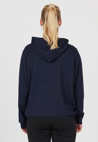 Marinblå tröja med huva, långa ärmar och en avslappnad passform. Slät textur, minimalistisk design, inga synliga mönster eller detaljer.