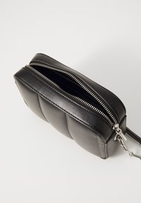 Borsa a tracolla in pelle nera con design trapuntato, compartimenti con doppia cerniera e dettagli in metallo argentato. Texture liscia e forma compatta.
