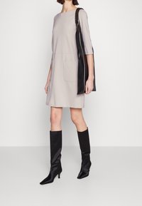 Ljusgrå klänning med trekvartslång ärm, två framfickor, matchad med svarta knähöga stövlar och en svart axelväska.