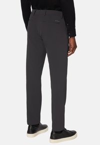 Grijze slim-fit broek van lichte stof, met een achterzak met een logo en gecombineerd met zwarte sneakers voor contrast.