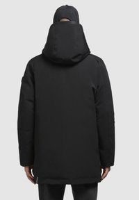 Sort polstret jakke med høj krave og hætte. Glat tekstur, let oversized pasform, synlig syning og lynlåsdetalje ved kanten.