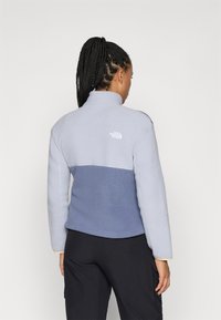 Fleece bunda vo svetlom a tmavom modrom, s vysokým golierom a logom na chrbte. Mäkkučký materiál s voľným strihom.