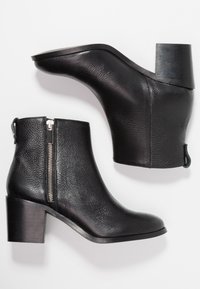 Stivaletti in pelle nera con finitura testurizzata, cerniera laterale e tacco spesso. Presentano una punta arrotondata e una sottile linguetta sul retro.