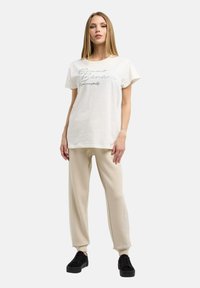 Vit t-shirt med korta ärmar och en tryckt logotyp, ihopparad med beigefärgade löst sittande byxor. Svarta kanvas sneakers fulländar looken.