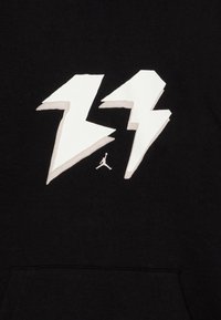 Czarna bluza z kapturem z dużym graficznym motywem białej błyskawicy oraz logo Jumpman w bieli poniżej. Miękka, gładka tekstura materiału.