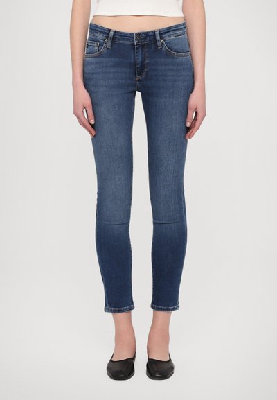 Schnelle Jeans aus dunkelblauem Denim mit hohem Bund, fünf Taschen und einer leichten Ausbleichung an den Oberschenkeln, kombiniert mit schwarzen Ballerinas.