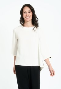 Top bianco fluente con maniche tre quarti e scollatura arrotondata, abbinato a pantaloni neri; trama liscia, orlo dritto.