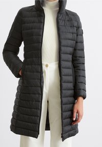 Polstret sort lang frakke med høj krave, der har et horisontalt quiltet design, lynlåslukning og to sidelommer. Glat tekstur.