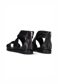 Zwarte leren sandalen met verstelbare banden, open ontwerp en een rits aan de zijkant. De zool is plat met minimale profiel voor comfort.