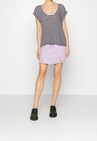 Pruhované tričko s krátkým rukávem v námořnické modré a bílé barvě, spárované s lila mini sukní s postranními rozparky. Černé nazouvací boty dokončují celý outfit.