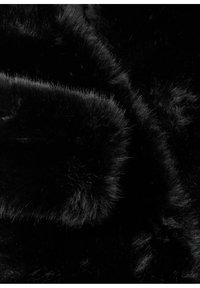 Tissu en fausse fourrure noire doux, dense et brillant, avec des fibres visibles et de subtils plis créant des textures et des ombres variées.
