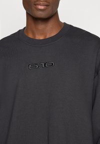 Tamsiai pilkas džemperis su ribbitu apvaliu kaklu ir ant krūtinės siuvinėtu „5.10“ logotipu, pagamintas iš sklandžios, tekstūruotos medžiagos.