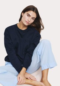 Mörkblå sweatshirt med "WEEKEND" präglat, i kombination med ljusblå, löst sittande byxor som visar mjuk bomullstextur och avslappnad passform.
