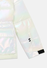 Manga de chaqueta inflable iridiscente con un gran bolsillo, puños elásticos y detalles de acento en negro. Textura suave y brillante con un acabado reflectante.