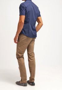 Camicia a maniche corte blu navy con pois bianchi, abbinata a pantaloni beige e scarpe grigie. La camicia presenta un colletto standard e una vestibilità comoda.