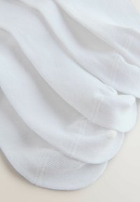 Białe bawełniane skarpetki o gładkiej fakturze, z prążkowanym wzorem i wzmocnionymi palcami. Ułożone warstwowo, zachodząc na siebie.