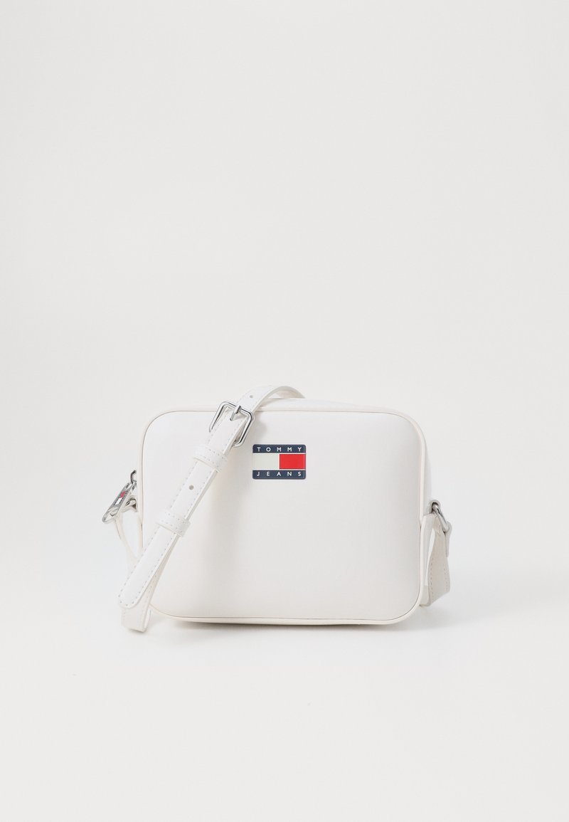 Borsa crossbody sintetica bianca con forma rettangolare, tracolla regolabile e un piccolo etichetta con logo che presenta accenti rossi e blu.