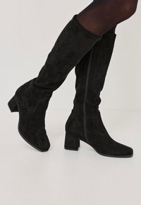 Mustat mokkasuuritossut, joissa on neliömäinen korko ja sivuvetoketju. Säilyttää tyylikkään muodon ja sileän tekstuurin.