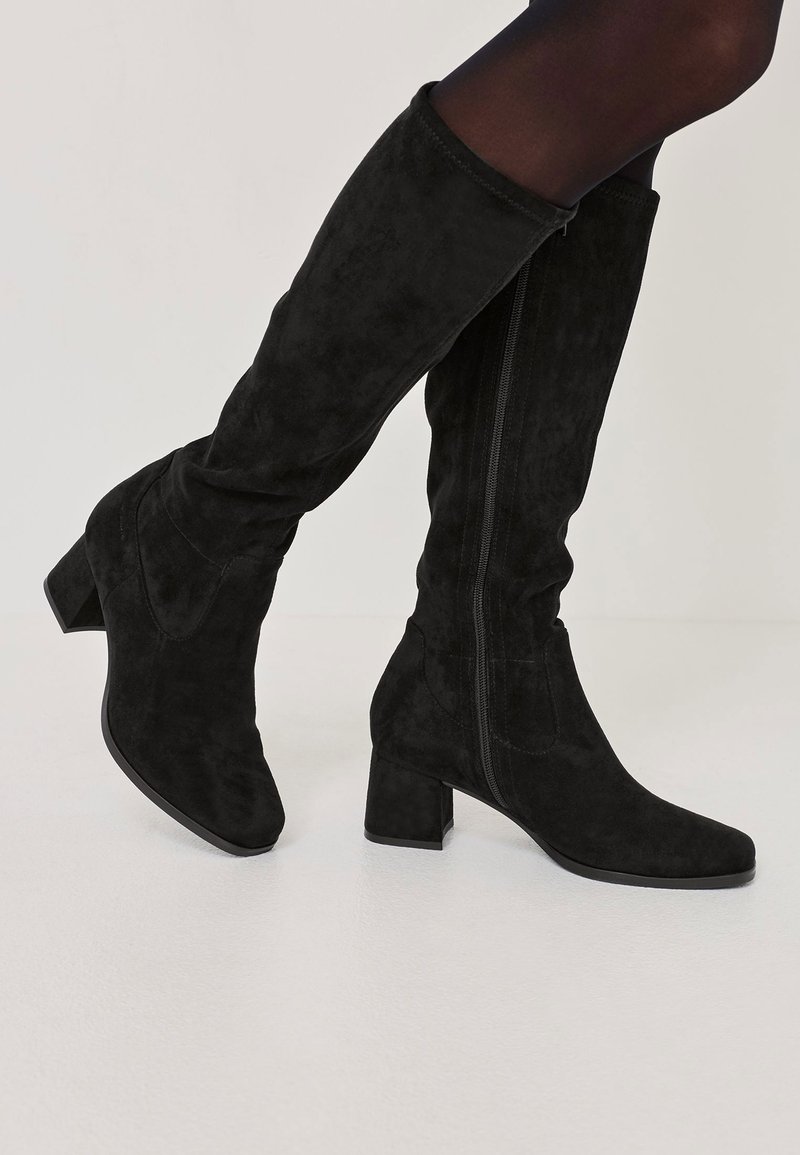 Mustat mokkasuuritossut, joissa on neliömäinen korko ja sivuvetoketju. Säilyttää tyylikkään muodon ja sileän tekstuurin.