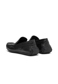 Zapatos negros de piel sin cordones que presentan una parte superior texturizada, un perfil bajo, punta redonda y suela de goma con un diseño de banda de rodadura para mayor tracción.