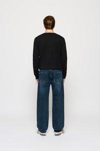 Camisa negra de manga larga combinada con unos vaqueros de mezclilla oscuros y holgados. El conjunto se completa con unas zapatillas blancas y negras con estampado.
