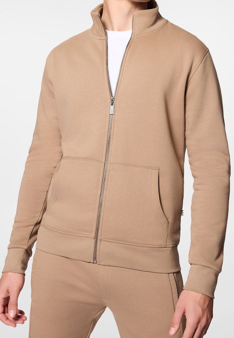 Felpa beige con zip, colletto alto, maniche lunghe, tasche frontali e polsini a coste, realizzata in un morbido tessuto testurizzato.